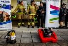 Sprzęt strażacki leży przed remizą. Za nim widoczni są strażacy.