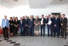 Wspólne pamiątkowe zdjęcie z udziałem kilkunastu osób, przedstawicieli samorządu, biznesu i instytucji, biorących udział w uroczystym podpisaniu umowy rozpoczynającej drogową inwestycję