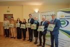 Zdjęcie pamiątkowe. Uczestnicy uroczystego przekazania pojazdu prezentujący otrzymane od strażaków ochotników obrazy przedstawiające wóz strażacki