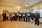 Zdjęcie pamiątkowe. Uczestnicy uroczystego przekazania pojazdu prezentujący otrzymane od strażaków ochotników obrazy przedstawiające wóz strażacki