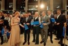 Osoby biorące udział w przecięciu wstęgi prezentujący z uśmiechem jej pocięte fragmenty 