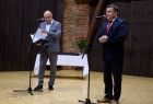 Wojciech Skruch stoi przy mikrofonie. Obok stoi mężczyzna.