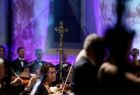 Metalowy, ozdobny krucyfiks stojący pomiędzy artystami w trakcie koncertu