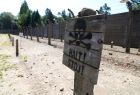 Widok na obozowe druty i historyczną drewnianą tabliczkę z wizerunkiem czaszki i skrzyżowanych piszczeli oraz napisem: Halt! Stój! 
