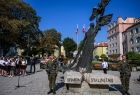 Żołnierze stoją na warcie przed pomnikiem z napisem Ofiarom Stalinizmu. Obok widoczna młodzież szkolna.