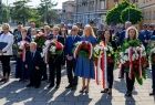 Uczestnicy wydarzenia stoją na placu. W tle zabytkowe budynki.