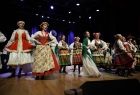 Kilkunastoosobowa grupa artystów w barwnych strojach ludowych podczas występu przed publicznością 