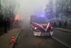 Nowy wóz strażacki jedzie po ulicy. Wokół jest dym z odpalonych racy.