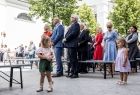 Dwie dziewczynki stojące na placu przed grupą osób.