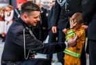 Marszałek Łukasz Smółka przyklęka przy małym chłopcu w strażackim uniformie