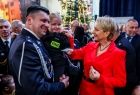 Marszałek Łukasz Smółka w galowym strażackim mundurze trzymający na ręku małą dziewczynkę. Tuż obok Iwona Gibas z Zarządu Województwa Małopolskiego