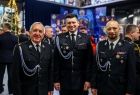 Marszałek Łukasz Smółka w galowym strażackim mundurze stojący wraz z dwoma strażakami 