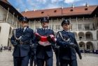 Policjanci w galowych mundurach niosący złożoną biało-czerwoną flagę