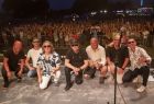 muzycy siedzą na scenie, przed fotografem