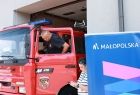 Przygotowania do wizyty. Strażak wysiadający z wozu bojowego OSP Brzeszcze, obok baner Małopolski