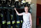 Iwona Gibas z zarządu województwa na tle rzędu strażackich bojowych uniformów