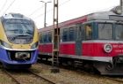 Dwa pociągi stoją na torach, po lewej stoi nowy pociąg Kolei Małopolskich, po prawej stary pociąg.