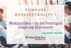 Hasło na jasnym tle "Konkurs Rozstrzygnięty". Niżej tekst: Małopolska- tu technologia staje się biznesem. Sprawdź wyniki. W tle młodzi ludzie przy stole przybijający sobie rękę w górze.