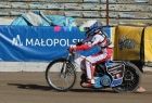 Żużlowiec jedzie na motocyklu po torze. Za nim widoczny napis Małopolska.