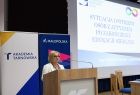 Kobieta mówiąca do mikrofonu. W tle slajd z napisem "Sytuacja i potrzeby osób z autyzmem po zakończeniu edukacji szkolnej. Mgr Elżbieta Wzorek - psycholog".