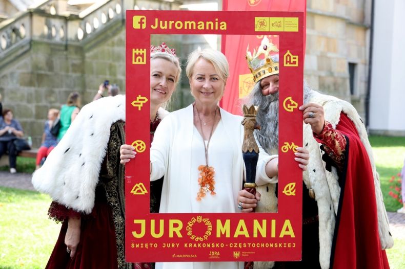 Iwona Gibas z zarządu województwa trzyma w rękach planszę z napisem Juromania. Obok stoi król i królowa. Za nimi widoczny klasztor na Skałce.