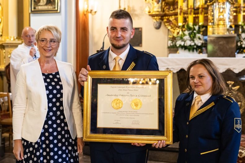 Przedstawiciele Amatorskiej Orkiestry Dętej Głębowice oraz Iwona Gibas z zarządu województwa prezentują wspólnie prestiżową nagrodę samorządu województwa małopolskiego