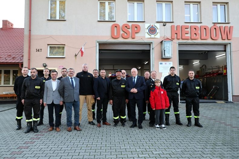 Uczestnicy wydarzenia stoją przed remizą z napisem OSP Hebdów.