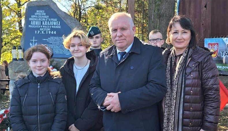 Wicemarszałek Ryszard Pagacz stoi z ludźmi. Za nimi widoczny pomnik.