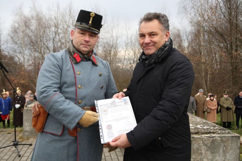 Arkadiusz Wrzoszczyk trzyma w rękach dokument. Obok stoi mężczyzna w historycznym mundurze.