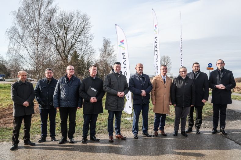 Uczestnicy wydarzenia stoją przy drodze. Za nimi widoczne banery z napisem Małopolska.