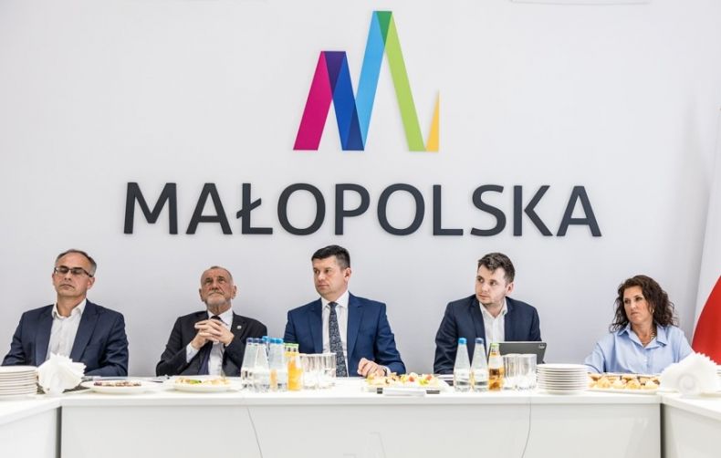 Marszałek Łukasz Smółka siedzi z ludźmi w sali obrad zarządu. Za nimi logo Małopolska.