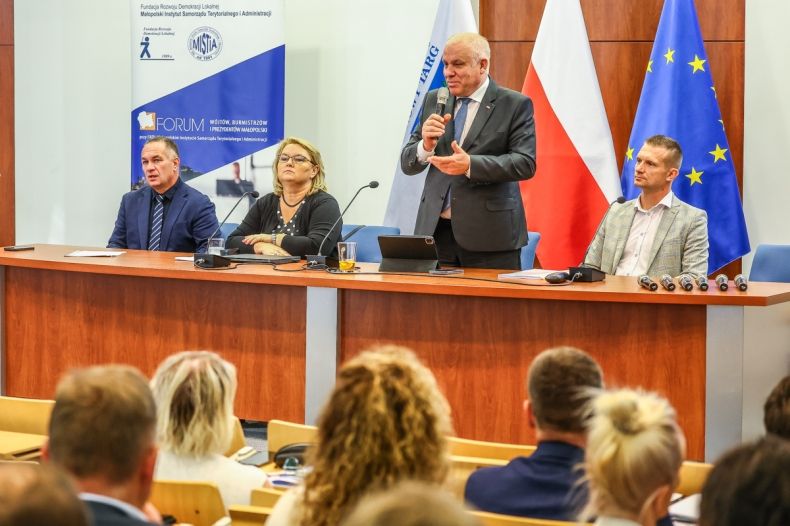 Wicemarszałek Ryszard Pagacz stoi przy stole. Obok siedzą inni ludzie.