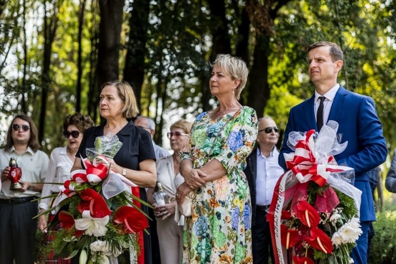 Iwona Gibas z zarządu województwa, Teresa Jankowska wicestarosta powiatu oświęcimskiego oraz Łukasz Kobielusz zastępca burmistrza Brzeszcz stojący z kwiatami przed pomnikiem upamiętniającym ofiary podobozu KL Auschwitz - Jawischowitz