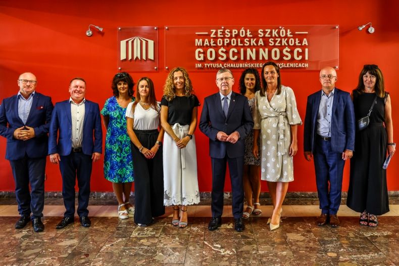 Zdjęcie grupowe na tle czerwonej ściany z logotypem Małopolskiej Szkoły Gościnności.