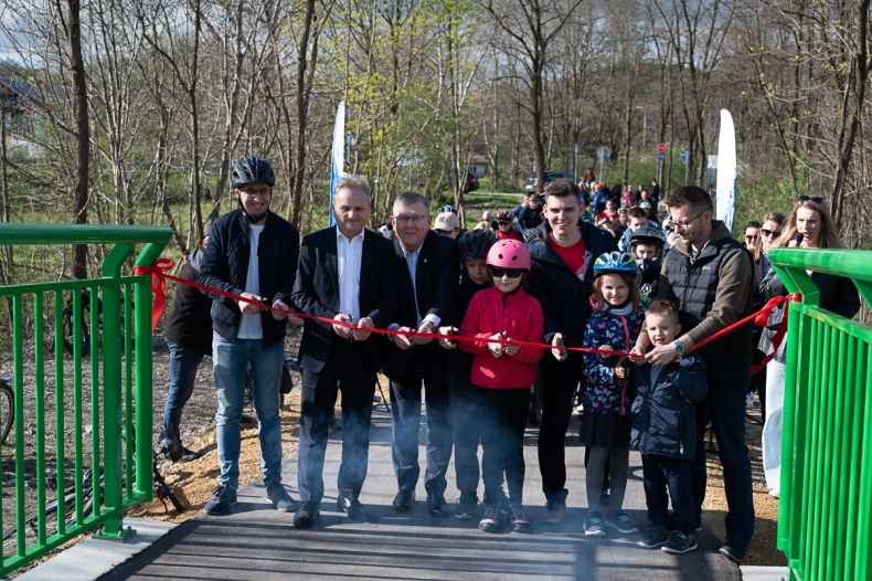 Uczestnicy wydarzenia przecinają czerwoną wstęgę na moście.