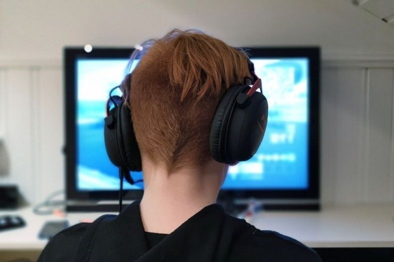 Chłopiec siedzi przed monitorem. Ma na uszach słuchawki.