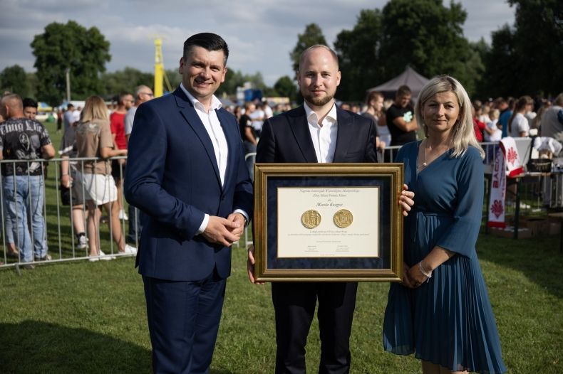 Marszałek Łukasz Smółka. Obok mężczyzna trzymający złoty medal i kobieta w zielonej sukience.
