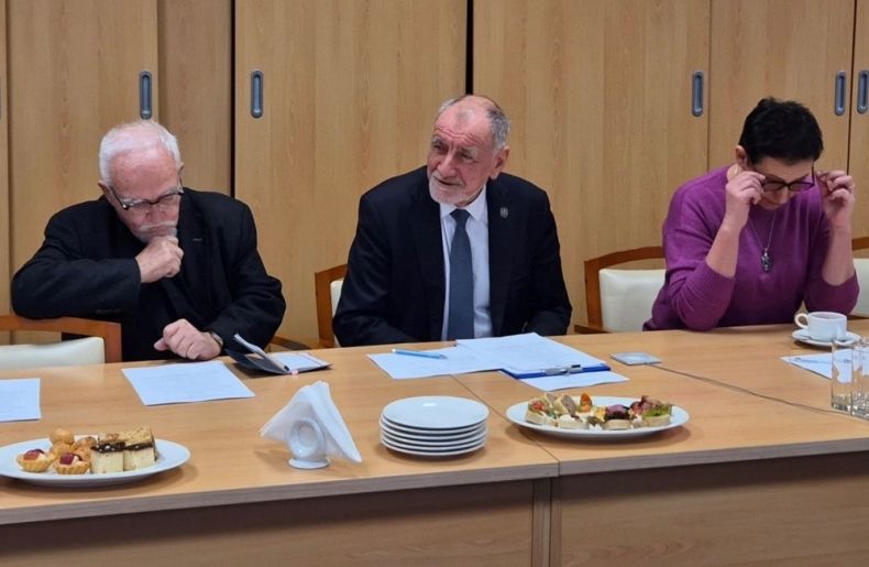 Przewodniczący Jan Tadeusz Duda siedzi przy stole. Obok siedzi mężczyzna i kobieta.