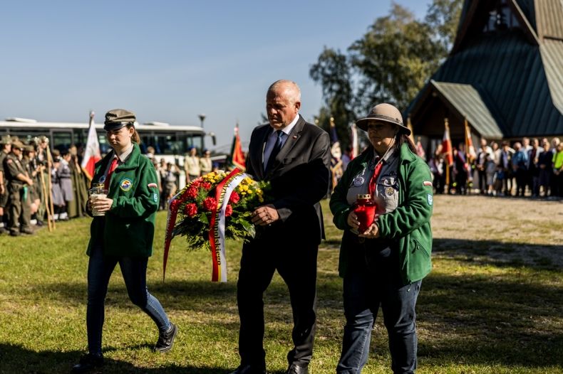 Wicemarszałek Ryszard Pagacz idzie przed pomnik w towarzystwie harcerzy. W rękach trzyma kwiaty.