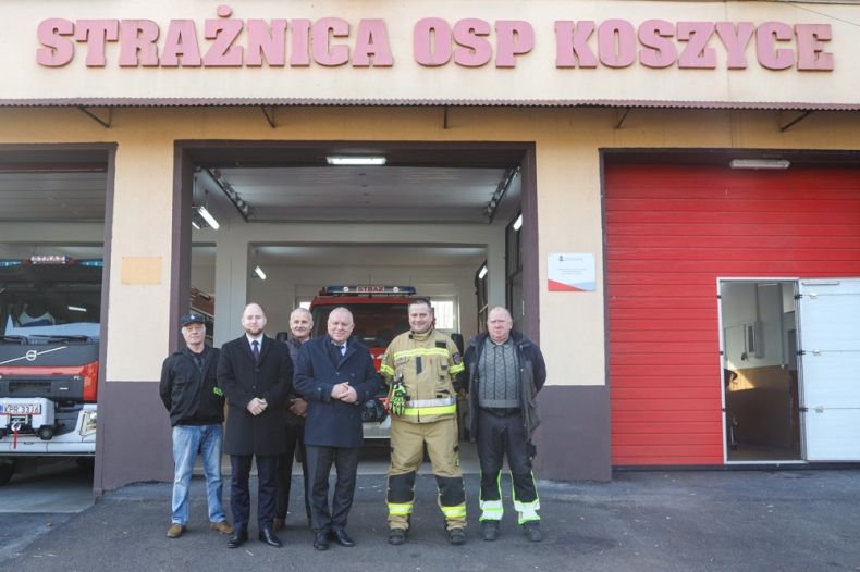 Uczestnicy wydarzenia stoją przed remizą z napisem OSP Koszyce.