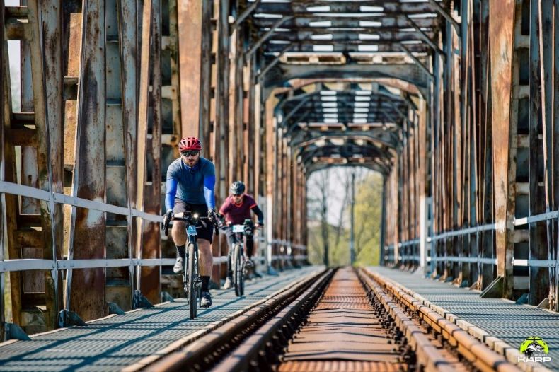 Dwóch rowerzystów jedzie mostem kolejowym.
