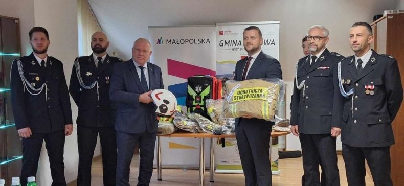 Wicemarszałek Ryszard Pagacz stoi ze strażakami w sali.