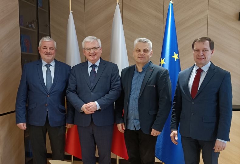 Grupa osób stoi na tle flag