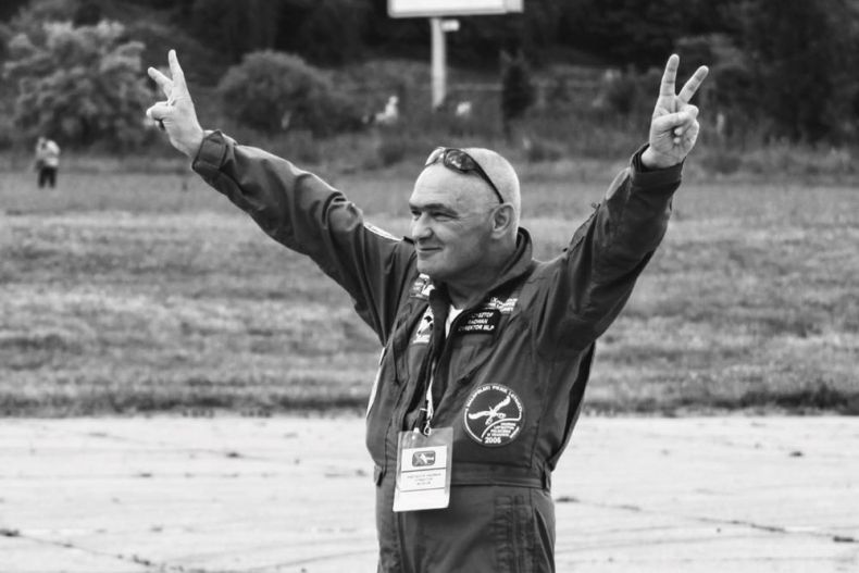 Krzysztof Radwan ubrany w strój lotnika stoi na pasie startowym i podnosi ręce do góry.