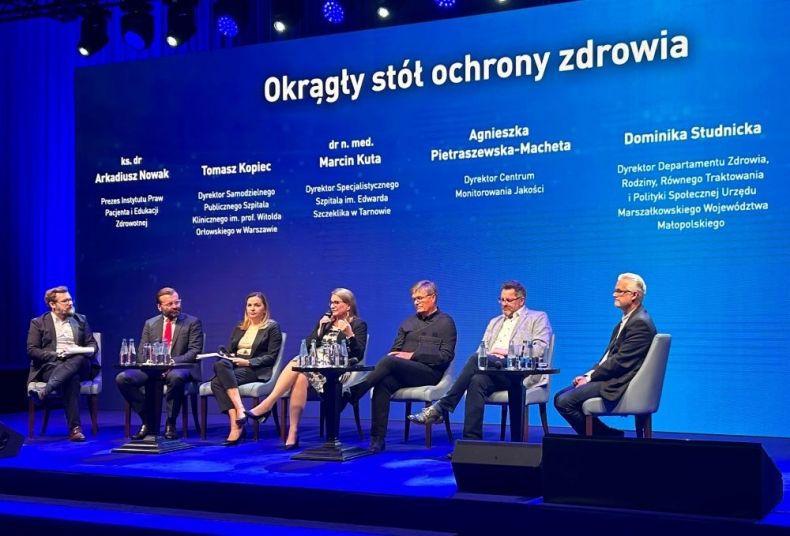 Ludzie siedzą na scenie. Na niebieskim tle widoczny biały napis Okrągły Stół Ochrony Zdrowia.