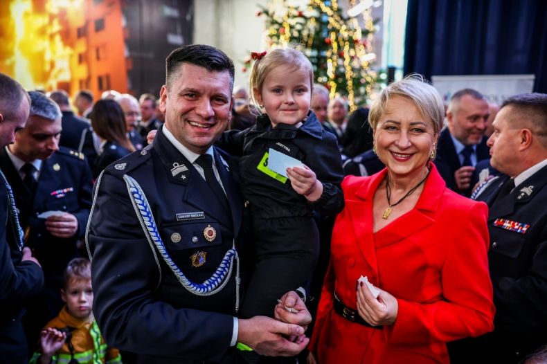 Marszałek Łukasz Smółka w galowym strażackim mundurze trzymający na ręku małą dziewczynkę. Tuż obok Iwona Gibas z Zarządu Województwa Małopolskiego