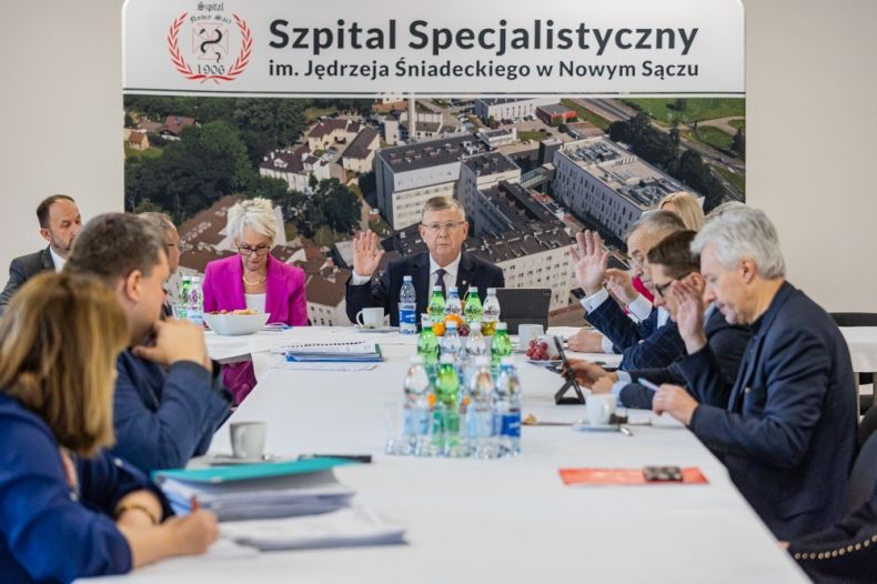Grupa ludzi przy stole głosująca przez podniesienie ręki. 