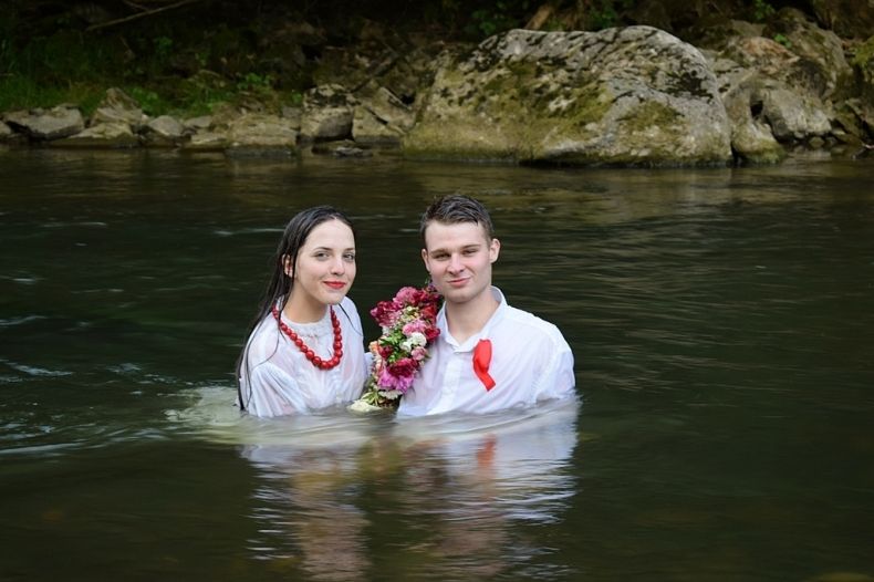 Zdjęcie kolorowe-dziewczyna i chłopak zanurzeni w rzece, trzymają wianek z kwiatów