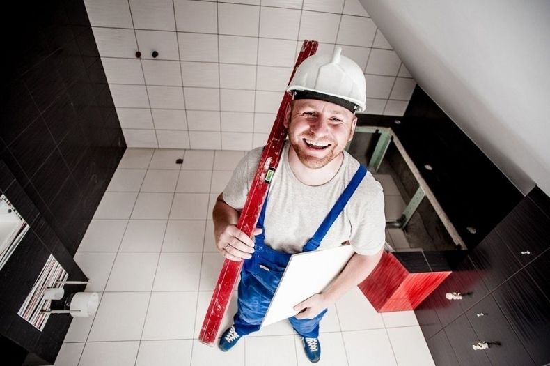 Uśmiechnięty robotnik trzyma w ręku czerwoną poziomicę.