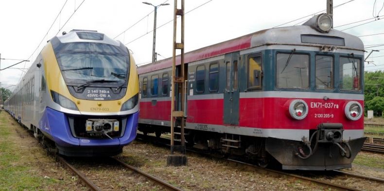 Dwa pociągi stoją na torach, po lewej stoi nowy pociąg Kolei Małopolskich, po prawej stary pociąg.